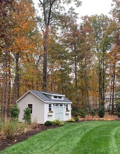 a small white shed sitting in the middle of a lush green field next to trees