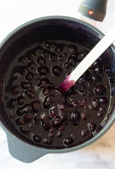 a pot filled with black olives on top of a white counter next to a spatula