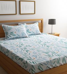 a bed with blue and green leaves on it in front of two framed pictures above the headboard