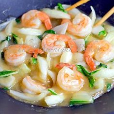 some shrimp and noodles are being cooked in a wok with chopsticks on the side