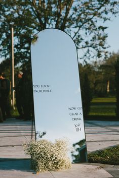 a large mirror sitting on the side of a sidewalk next to a planter filled with baby's breath