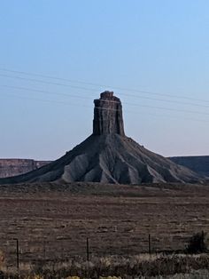 a large rock formation in the middle of a desert with power lines above it and a sky background