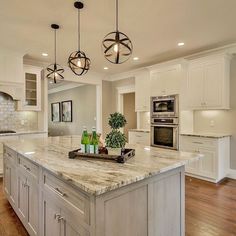 a large kitchen with an island in the middle and two lights hanging from the ceiling