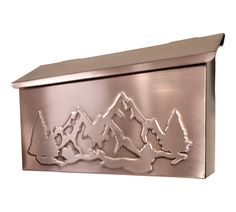 a metal mailbox with mountains and trees on the front, shown in polished bronze