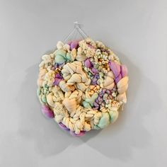 a circular object made out of shells on a white wall hanging from a metal hook