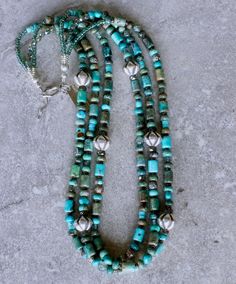 This good-looking Necklace showcases 3 strands of Mixed Turquoise, including 6-by-9mm Drum Beads, 4-by-6mm Rondelles, 6mm Triangles and 4mm Heishi. The Turquoise displays a variety of blue and green hues, creating a color palate that is visually engaging. It is paired with several other complementary elements, notable of which are the 11-by-12mm Hill Tribe Silver Ridged Bicones. The Bicones are beautifully crafted and polished to a soft luster. Other elements are comprised of: 6mm green Rutilate Southwest Design, Hill Tribe Silver, Color Palate, Green Hues, Color Depth, Rutilated Quartz, Toggle Clasp, Strand Necklace, Triangles