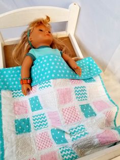 a doll laying on top of a bed next to a blue and white quilted blanket