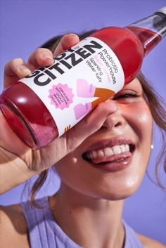 a woman is holding up a bottle of cherry juice to her face and smiling at the camera