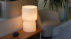 a white lamp sitting on top of a wooden table next to a chair and potted plant