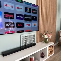 a flat screen tv sitting on top of a white shelf next to a vase with flowers