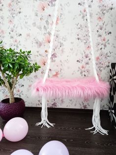 a pink hammock hanging from a tree with balloons and a potted plant