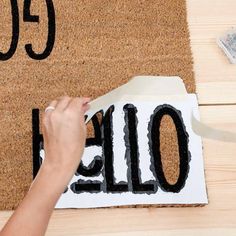 someone cutting out the word hello in front of a door mat with scissors and tape