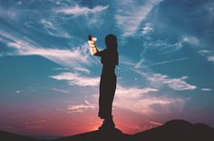 a person standing on top of a hill flying a kite in the sky at sunset