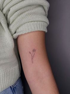 a woman's arm with a small flower tattoo on the back of her left arm