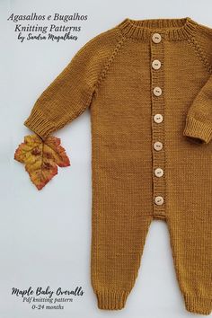 a baby's knitted sweater with buttons and a leaf laying on the ground