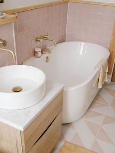 a white bath tub sitting next to a wooden cabinet in a pink tiled bathroom with gold faucet