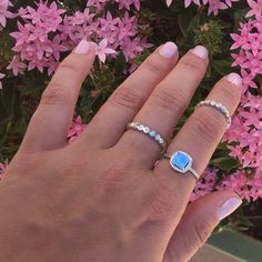 a woman's hand with two rings on it and pink flowers in the background