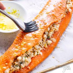 a person holding a fork and spoon over a piece of salmon