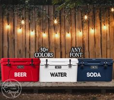 three coolers sitting next to each other in front of a fence with string lights