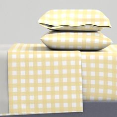 three pillows are stacked on top of each other with yellow and white plaid sheets in the background