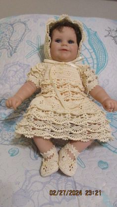 a baby doll sitting on top of a bed wearing a dress and bonnet with crochet