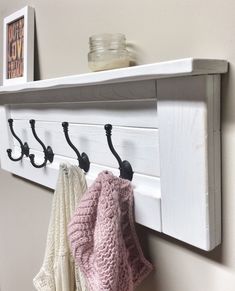 a white coat rack with three coats hanging on it's hooks and two knitted sweaters