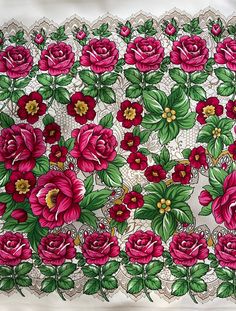 an embroidered tablecloth with red roses and green leaves on white lace, in front of a plain background