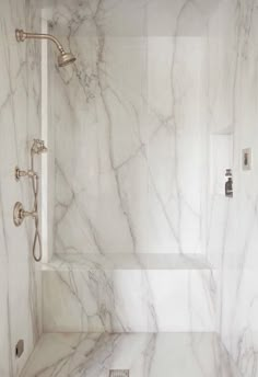 a bathroom with white marble walls and flooring, shower head and hand shower arm