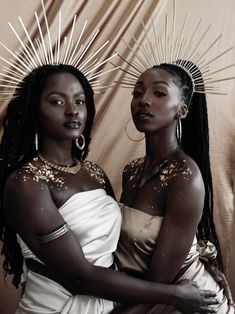 two african women in white dresses with gold decorations on their heads and arms, both wearing large hoop earrings