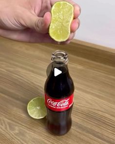 a person holding a lime over a soda bottle on a wooden table with a slice of lime in it