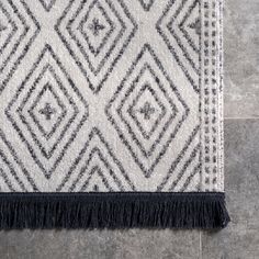 a black and white rug with fringes on the floor in front of a tile wall