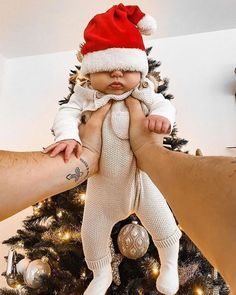 a baby wearing a santa hat is being held up by someone's arm and leg