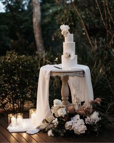 a white wedding cake sitting on top of a wooden table next to candles and flowers