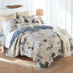 a bed covered in blue and white comforter next to a lamp on a wooden floor