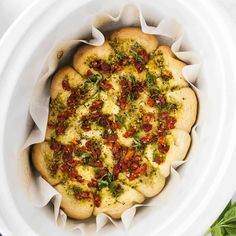 a pizza in a white bowl on top of a table next to some green leaves