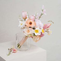 a bouquet of flowers in a glass vase on a white surface with a pink ribbon