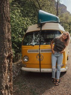 a woman standing in front of an old vw van with a surfboard on top