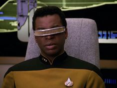 a man wearing a star trek uniform with glasses on his face and eye patch in front of him