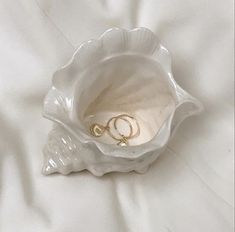 two gold wedding rings in a shell on a white bed sheet with a ring holder