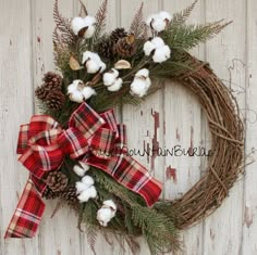 a wreath with cotton and pine cones is hung on a wooden wall next to a red plaid bow