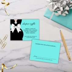 two business cards on a table with gold ribbon and blue envelopes next to it