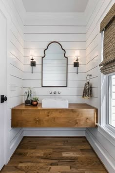 a white bathroom with wood flooring and a mirror on the wall above the sink