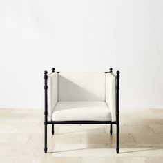 a white chair sitting on top of a tile floor next to a wall with a black frame