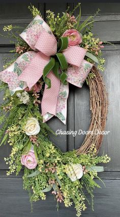 a wreath with pink flowers and green leaves on the front door is hanging from a wooden door