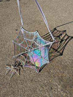 a spider web hanging upside down on the ground in front of a person's shadow