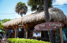 a wooden sign that reads the cottage sits in front of some palm trees