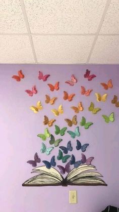 an open book sitting on top of a table next to a wall with butterflies flying out of it