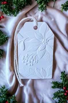 a white christmas ornament hanging from a string on a bed covered in holly