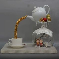 a glass teapot filled with gold and white decorations next to a cup on a saucer