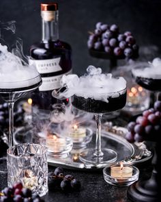 two glasses filled with liquid and ice on top of a table next to bottles of wine